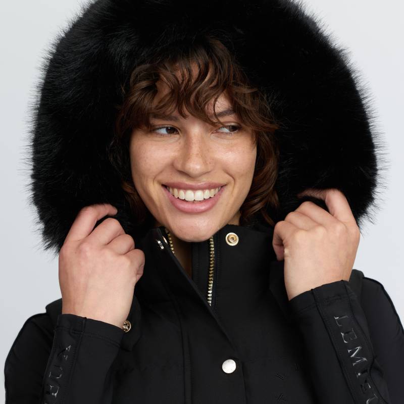 Smiling person in LeMieux Margot Hooded Gilet Black holding the hood with both hands.