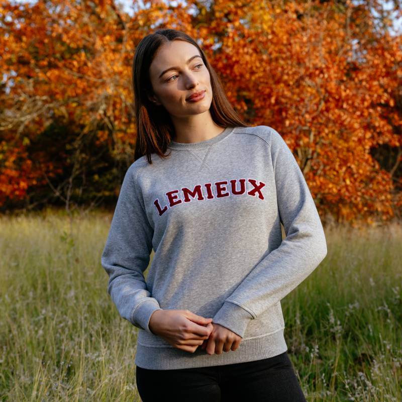 Woman in a grey LeMieux Vida Varsity Crew Neck Sweat stands in a field with autumn trees.