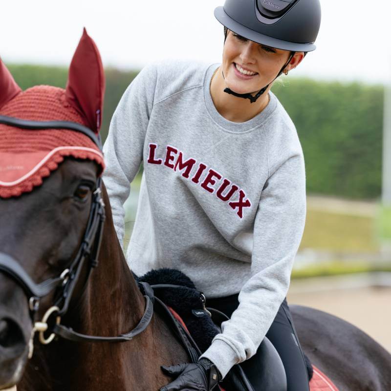 Smiling rider in helmet on horse wearing LeMieux Vida Varsity Crew Neck Sweat Grey Marl, red tack.