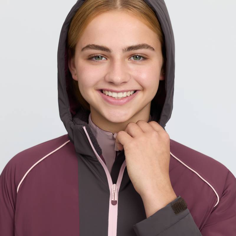 Smiling person in a hooded LeMieux Young Rider Bailey Waterproof Anorak Bramble, facing camera.