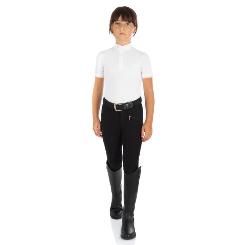 Child in Equestro Kasumi Black breeches, white shirt, and boots walks forward.