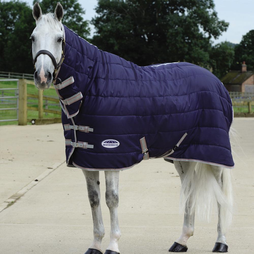 A white horse in a Weatherbeeta Comfitec 210D stable rug stands near a wooden fence.