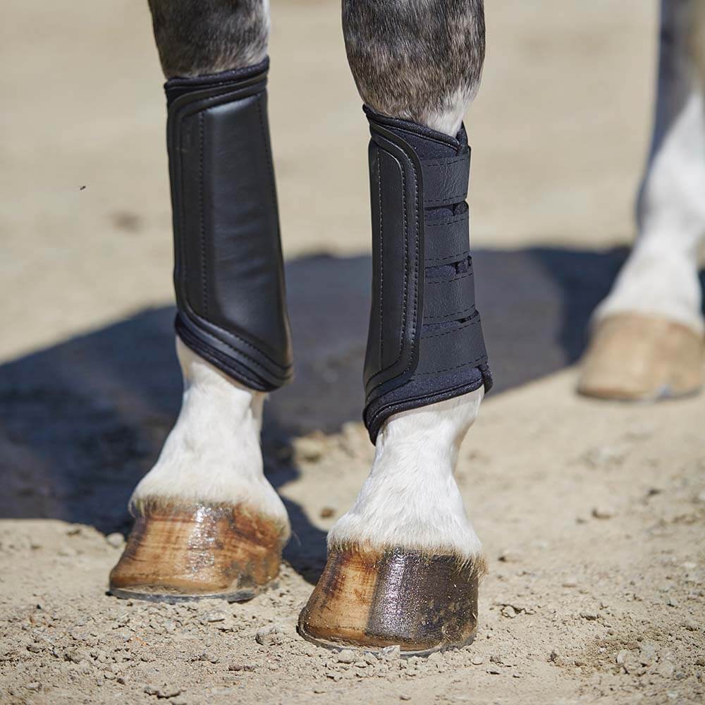 Close-up of horse’s legs in Weatherbeeta Single Lock Brushing Boots on a sandy surface.