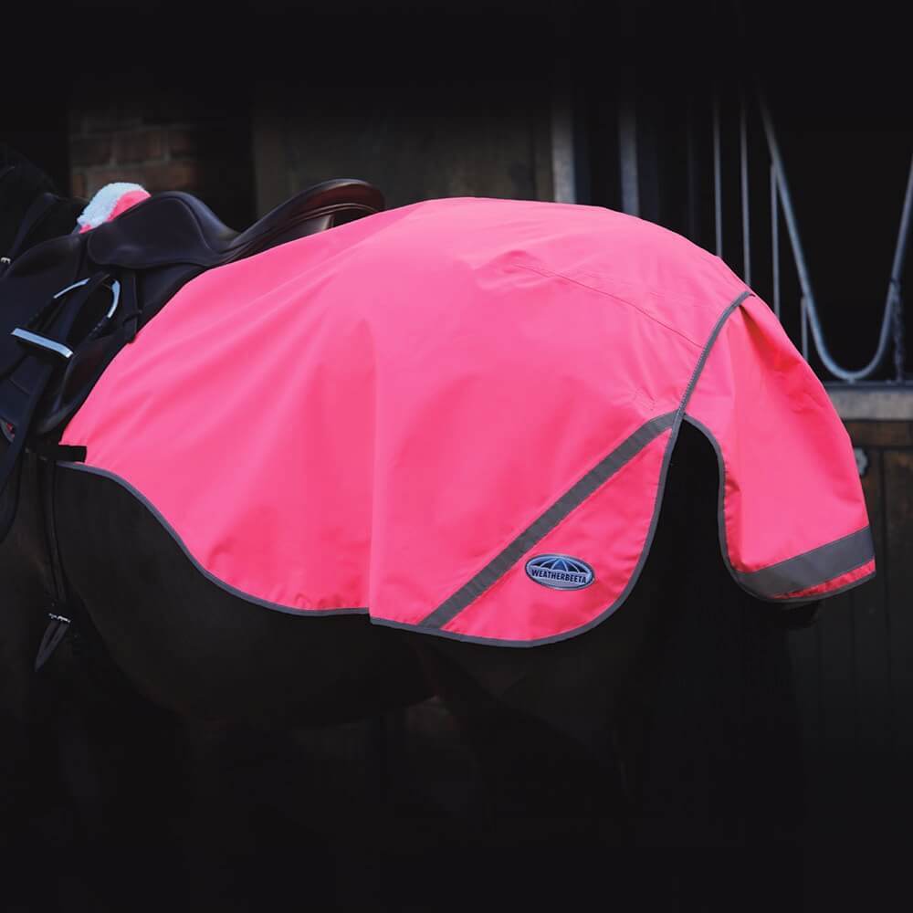 A horse wears a Weatherbeeta 300D Reflective Exercise Sheet Pink in a dimly lit stable.