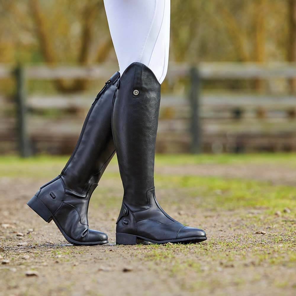 Person in black Dublin Arderin Tall Dress Boots and white pants stands on dirt outdoors.