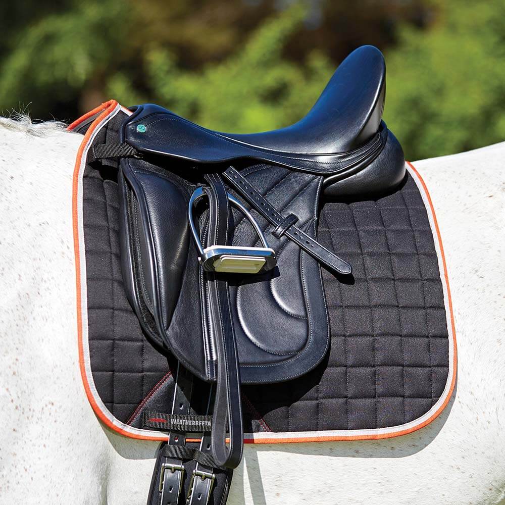 Black English saddle with stirrup on white horse, over a Weatherbeeta Therapy-Tec Dressage Pad.