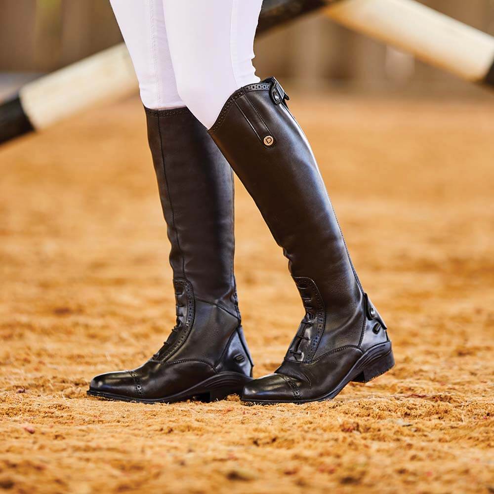Person wearing Dublin Evolution Tall Boots and white pants stands on sandy ground.