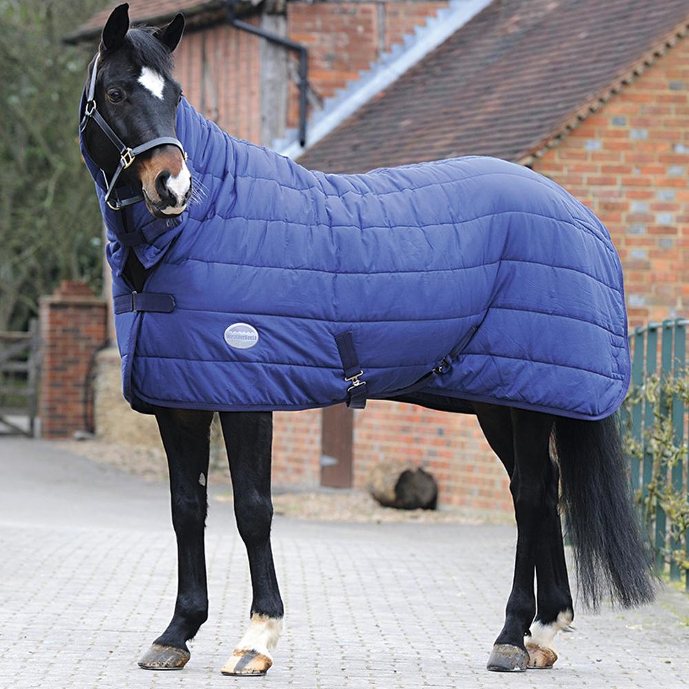 A black and white horse in a Weatherbeeta Under Rug Combo Neck stands on paving by buildings.