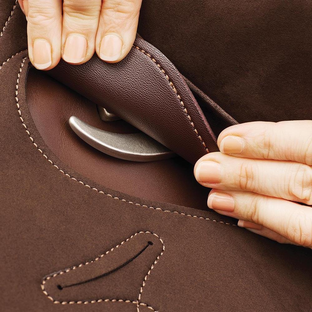 Hands lift a flap on brown leather, revealing a Wintec Pro Stock Hart Saddle underneath.