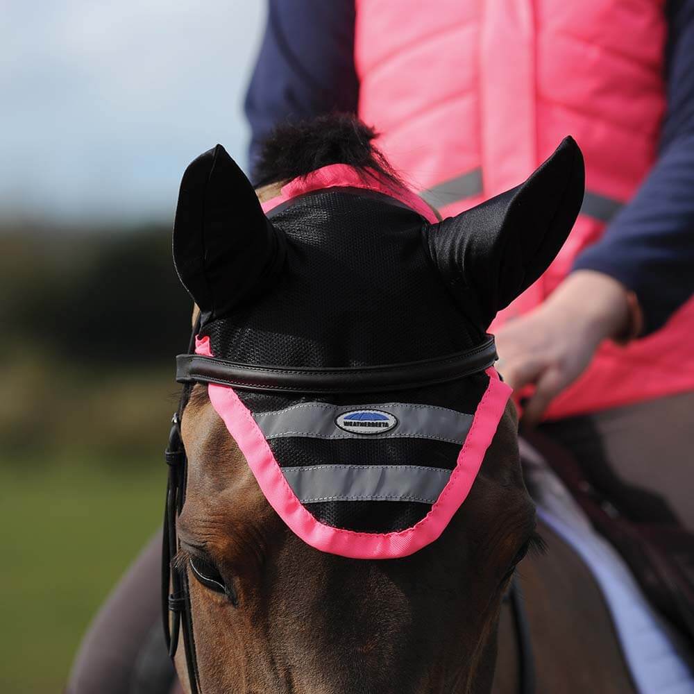 Person riding a horse with a Weatherbeeta Reflective Ear Bonnet Pink and matching vest.