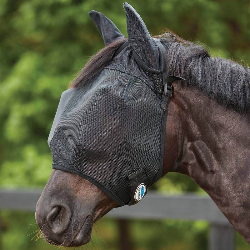 A horse wears the Weatherbeeta Comfitec Double Dart Deluxe Fly Mask With Ears, outside in greenery.