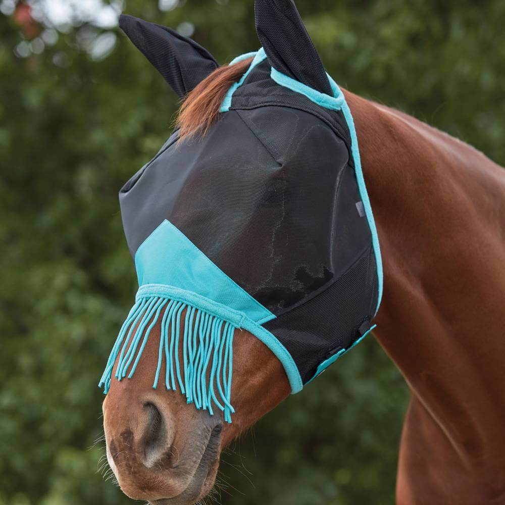 A brown horse wears a Weatherbeeta Comfitec Deluxe Fine Mesh Mask with Ears &amp; Tassels outdoors.