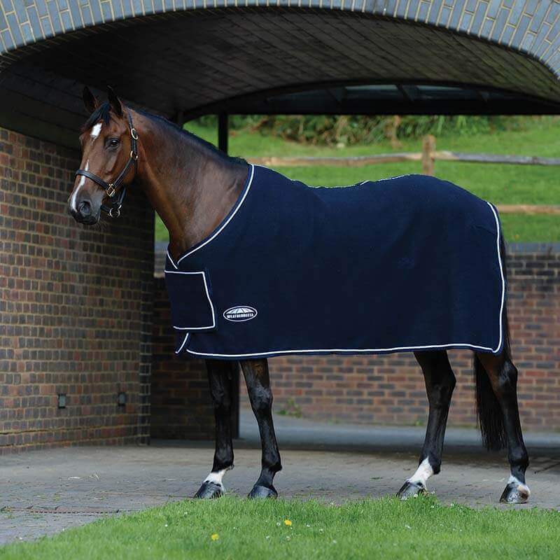 A brown horse in a navy/white Weatherbeeta Wool Show Sheet stands under a brick archway.