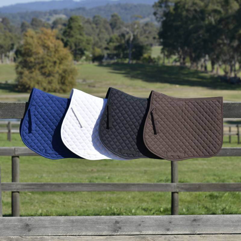 Four Saxon Defiant All Purpose Saddle Pads in black, blue, white, and brown on a fence.
