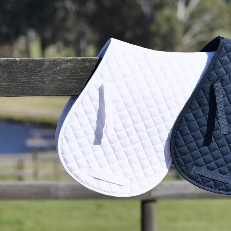 Saxon Defiant All Purpose Numnah White by Saxon hangs over a wooden fence outdoors.