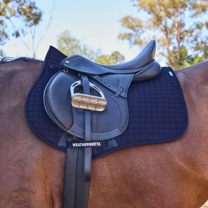 Navy Weatherbeeta Prime Air-Tec saddle pad on a brown horse with black saddle in sunlight.