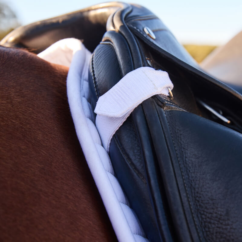 Close-up of a black saddle with a Weatherbeeta Prime Air-Tec white pad on a brown horse.