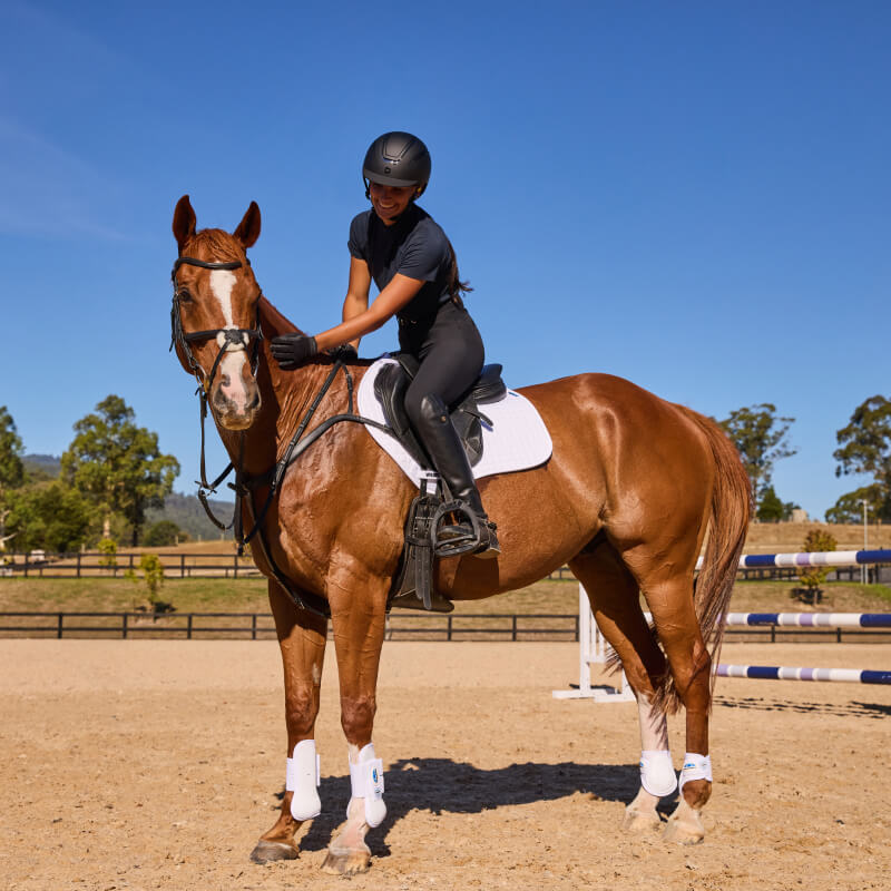 Smiling rider in black gear sits on a brown horse with a white Weatherbeeta saddle pad.