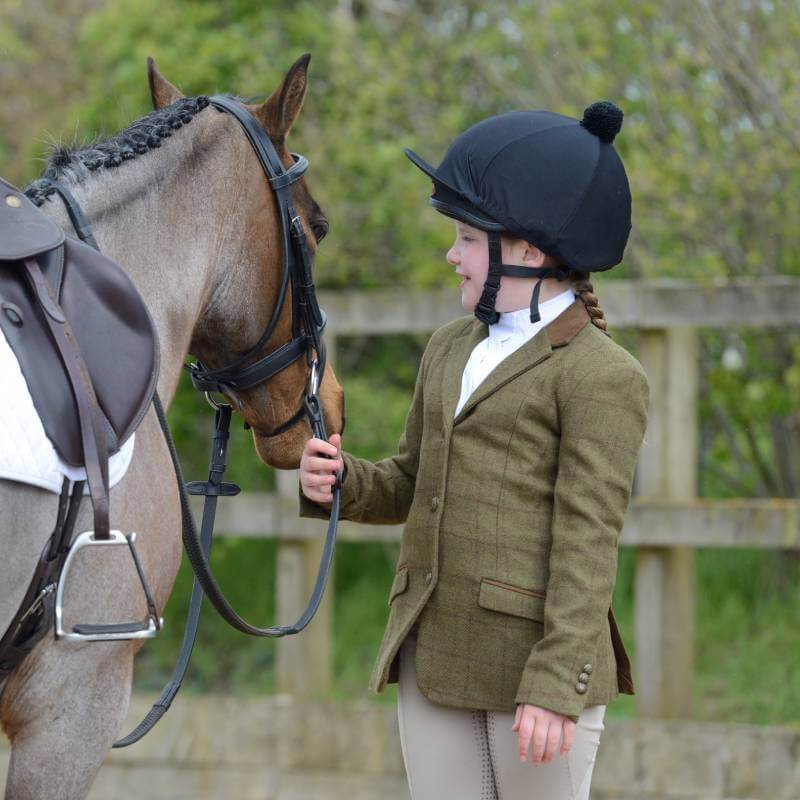 Child wearing a Dublin Albany Tweed Suede Collar Jacket pets a brown horse by a wooden fence.