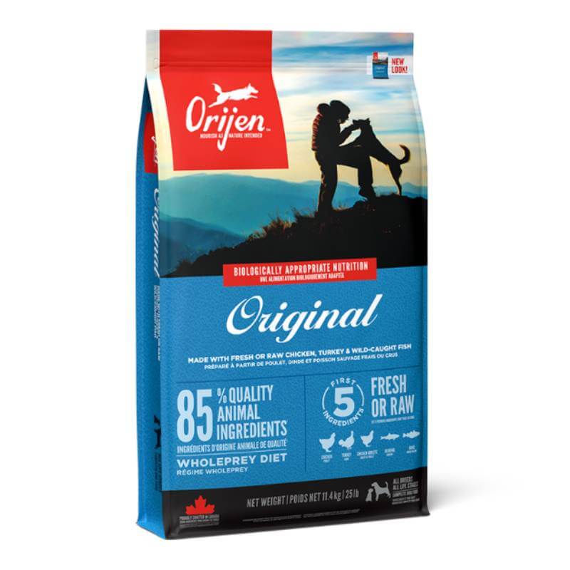 Orijen Original Grain-Free Dog Food bag features a person hugging a dog atop a mountain.