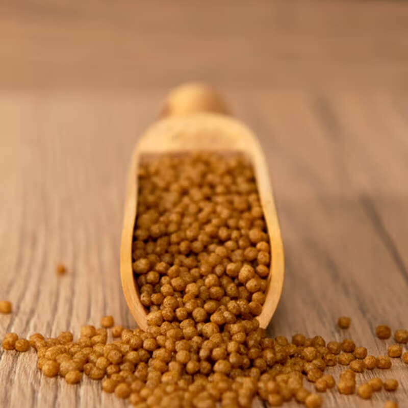 Psittacus Minor parrot food pellets spill onto a wooden surface from a wooden scoop.